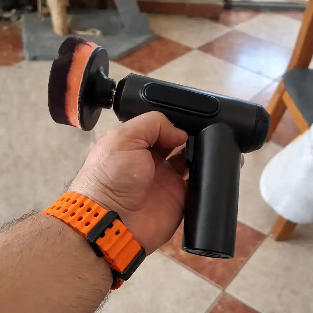 Hand holding a black power tool with an orange wristband on a tiled floor.