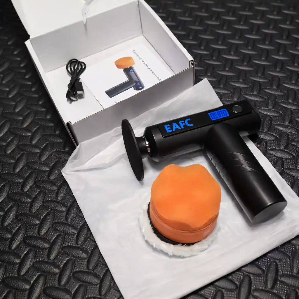 Car detailing tool set with black gun, orange pad, and digital display on a textured black surface.