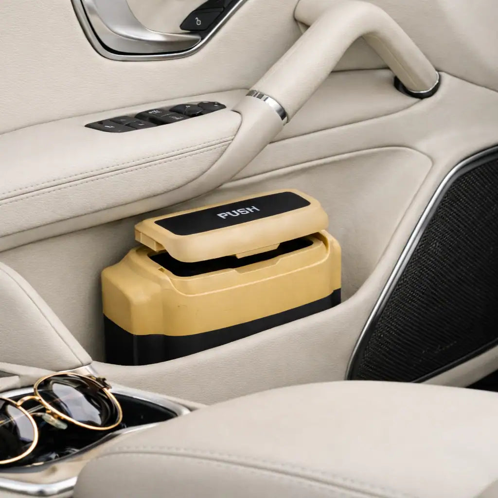 A premium trash bin with a “PUSH” lid sits in a beige car door pocket; sunglasses rest near the center console.
