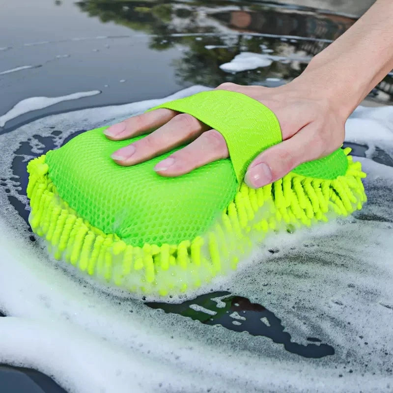 Close-up of car detailing: a neon green chenille microfiber mitt glides over suds on a shiny car hood.