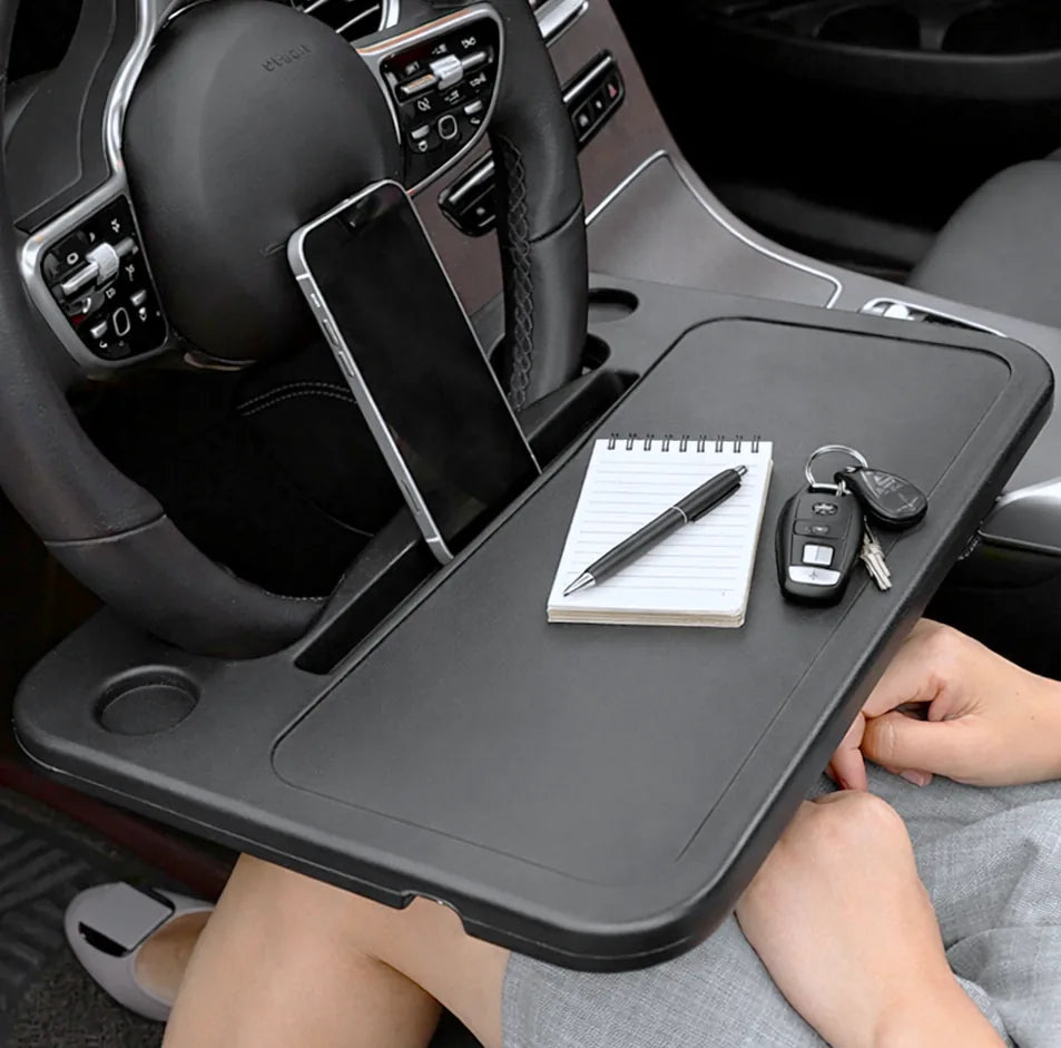 Car dashboard tray with phone, notebook, pen, and keys in a car.